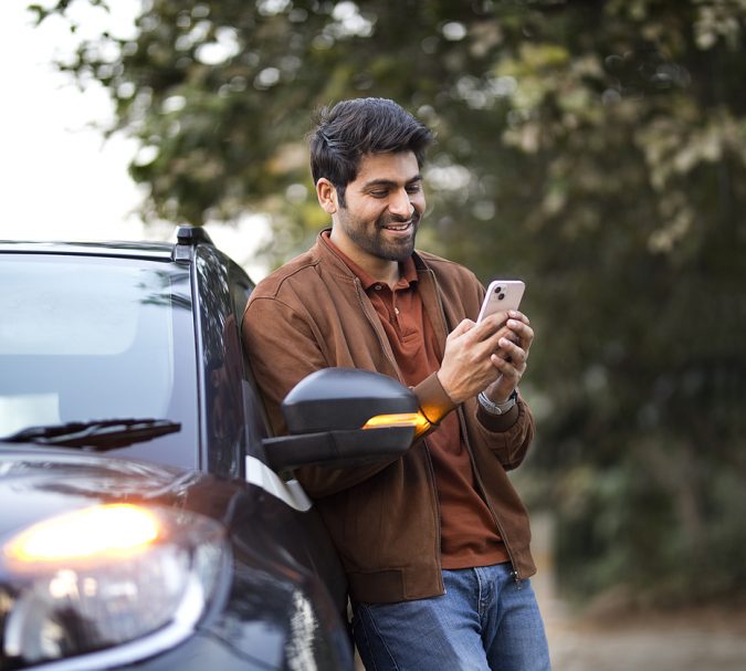 Smiling young man texting on mobile phone leaning on her car