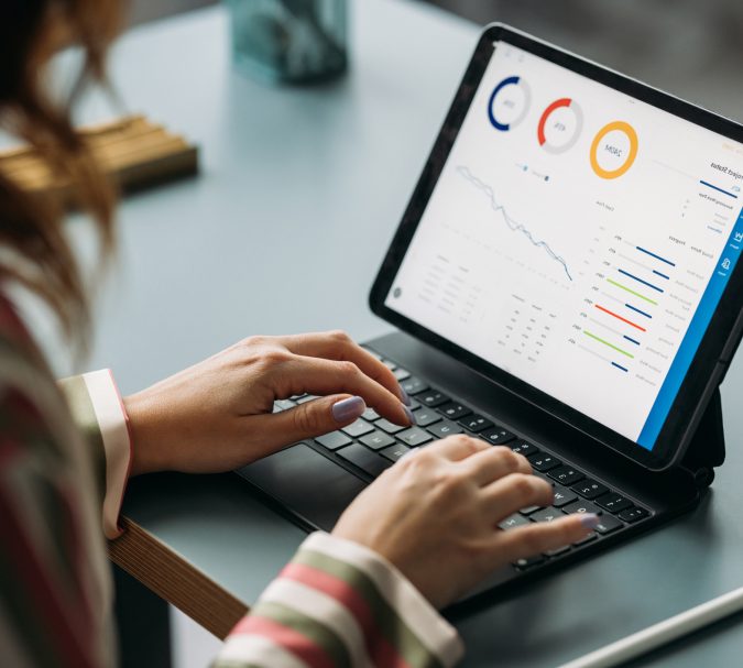 Woman in striped shirt working on tablet displaying colorful graphs and data analysis in a business environment.