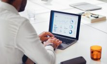 A businessman in a white shirt uses a laptop to analyze financial data and charts, focusing on business growth and strategy development in a modern office setting.